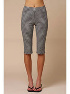 Woman wearing black and white gingham patterned capri pants with black strappy sandals against beige background