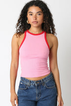 Woman wearing a sleeveless pink ringer tank top with red trim paired with blue denim jeans in a casual style