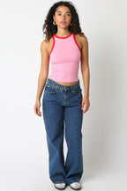 Woman wearing a sleeveless pink tank top with red trim paired with blue denim jeans in casual women's clothing style
