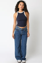 Woman wearing sleeveless navy tank top with white trim and high-waisted wide-leg blue jeans in casual style