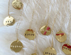 Gold-tone hand-stamped pendant necklaces with lowercase typewriter font on delicate chains on a soft white background