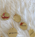 Close-up of gold hand-stamped round pendant necklaces with words like mood and bougie on delicate chains