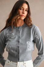Woman wearing a gray cropped knit cardigan with white embroidered dolphin, dog, and floral designs in women's clothing style.