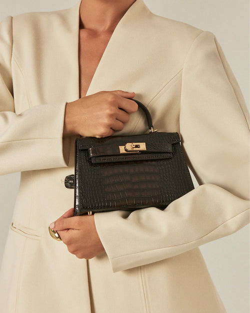 Woman in a cream blazer holding a black crocodile textured structured handle bag