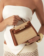 Woman holding a brown and woven handle bag wearing a white top and cream crochet skirt with gold bracelets
