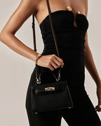 Woman wearing a strapless black top holding a small black leather handle bag with gold hardware