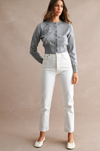 Woman wearing a gray embroidered cardigan with white high-waisted pants and white ballet flats against plain background