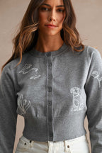 Woman wearing a gray button-up cardigan with white embroidered dolphin, dog, flower, and plant designs in women's clothing style.