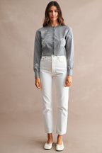 Woman wearing a gray embroidered cardigan with white high-waisted jeans, posing against a neutral background.