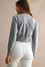 Woman wearing a fitted gray cardigan with white embroidered dog detail on the back, paired with white jeans.