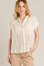 Woman wearing a short sleeve white crochet button-down shirt paired with beige pants in a neutral setting
