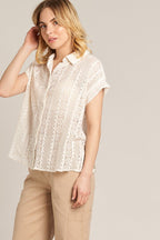 Woman wearing a short sleeve crochet button down shirt in white paired with light beige pants
