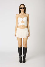 Woman wearing a white mini skirt with built-in shorts and black knee-high boots against a white background