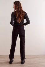Woman wearing black high-rise kick flare pants and black ribbed sweater standing against white wall