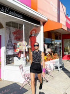 Woman in black sleeveless mini dress with sequin details walking past colorful boutique with outdoor seating and autumn decor