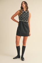 Woman wearing a black sleeveless mini dress with sequin details and collar, paired with knee-high socks and black shoes