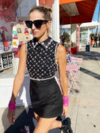 Woman wearing a black sleeveless mini dress with sequin details and a collar, accessorized with sunglasses outdoors