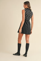 Woman wearing a sleeveless black mini dress with sequins on the upper back and black knee-high socks