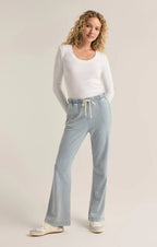 Woman wearing light blue knit denim pants with drawcord waist and white long sleeve top in a studio setting