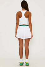 Woman wearing white pleated skirt with green waistband and white crop top, styled in casual sporty look