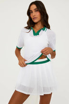 Woman wearing a white mesh pleated skirt and matching short-sleeve top with green trim in women's clothing.