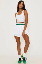 Woman wearing white pleated skirt with green waistband and white crop top paired with green sneakers in studio setting