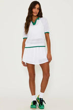 Woman wearing white mesh pleated skirt with built-in shorts and matching mesh top in women's clothing fashion.