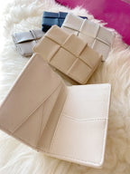 Collection of flat woven vegan leather wallets in neutral and dark colors, displayed on soft white fabric.