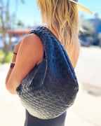 Woman carrying a black woven vegan leather bag outdoors, accessorizing her casual summer outfit and hat.