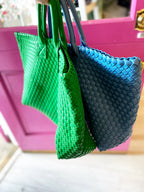 Close-up of green and blue woven vegan leather bags with handles, held in front of a pink door.