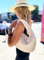 Woman in sunhat carrying a light woven vegan leather bag over shoulder outdoors in daytime