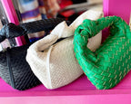 Three woven vegan leather bags in black, white, and green with zip closures displayed on a pink surface.