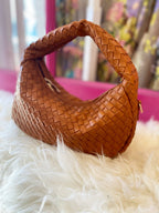 Brown woven vegan leather bag with curved handle resting on white faux fur surface in colorful setting