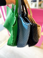 Hand holding four woven vegan leather bags in green, blue, black, and beige, suitable for women's clothing.