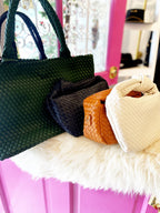 Four woven vegan leather bags in dark green, black, brown, and cream displayed on a white surface.