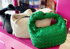Three woven vegan leather bags in green, white, and black displayed on a pink shelf for women's fashion.
