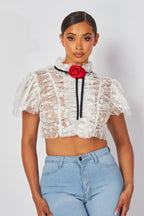 Woman wearing a white lace crop top with puff sleeves and red rosette detail paired with light blue jeans