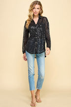 Woman wearing a black sequin button-up long sleeve top paired with light blue jeans and sandals in a studio setting.