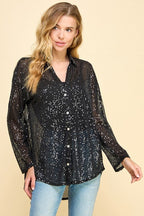 Woman wearing a loose fit black sequin button-up top with long sleeves and collar paired with light blue jeans