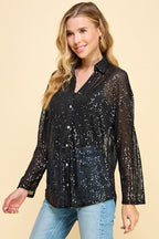 Woman wearing a loose fit black sequin button-up shirt with long sleeves and collar, styled with light blue jeans