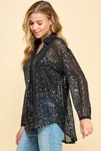 Woman wearing a loose fit, long sleeve black sequin button-up top paired with light blue jeans against beige background