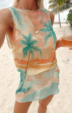 Woman wearing pastel tropical print sleeveless top and skirt set holding a glass of wine on the beach