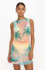 Woman wearing a sleeveless mini dress with a tropical sunset and palm tree print, perfect for women’s fashion.