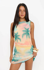 Woman wearing sleeveless mini dress with tropical sunset palm tree print in pastel colors
