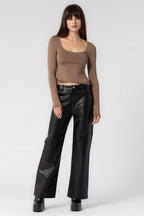 Woman wearing fitted long sleeve beige top and wide-leg black leather pants in casual women's clothing style