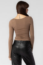 Woman wearing brown fitted long sleeve top and black leather pants, shown from the back in women's clothing style
