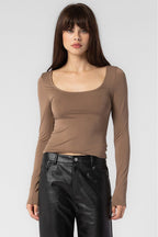Woman wearing a fitted brown long sleeve top paired with black leather pants in women's clothing fashion style.