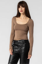 Woman wearing a fitted brown long sleeve top paired with black leather pants in a studio setting