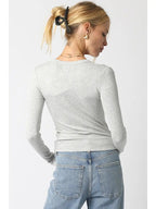 Woman wearing a fitted light gray ribbed long sleeve top paired with blue denim jeans, styled with hair clip and minimal jewelry