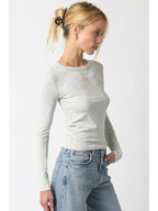 Woman wearing a fitted light gray ribbed long sleeve top paired with blue denim jeans in a side profile pose